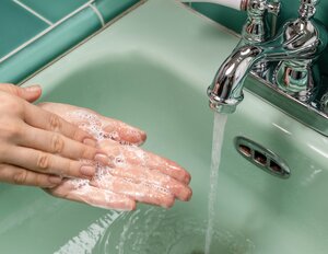 någon tvättar sina händer i ett handfat